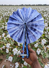 Load image into Gallery viewer, Blue tie-dye folding fan held by a hand against a cotton field