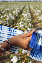 Load image into Gallery viewer, Person holding a blue tasseled tie-dye pouch against a cotton field