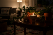 Cargar imagen en el visor de la galería, Candlelit scene in a dimly lit living room with plants and a wooden table.