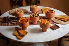 Carregar imagem no visualizador da galeria, Round table with terracotta bowls containing snacks on an African patterned table runner