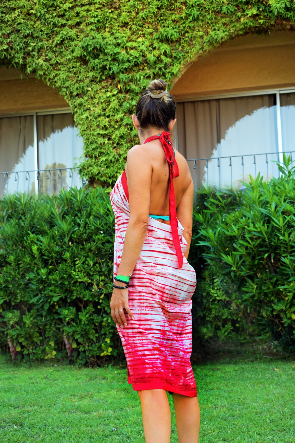 A woman wearing a red and white tie & dye wrap dress in a green garden.