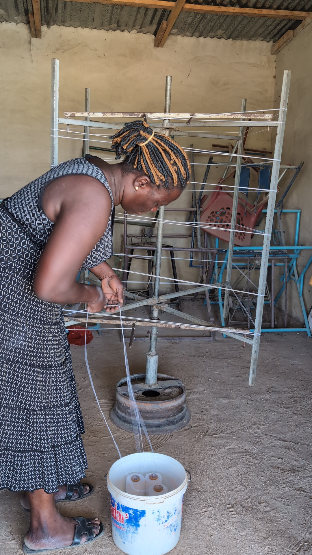 A woman preparing and winding cotton warp threads on a vertical frame in a workshop.