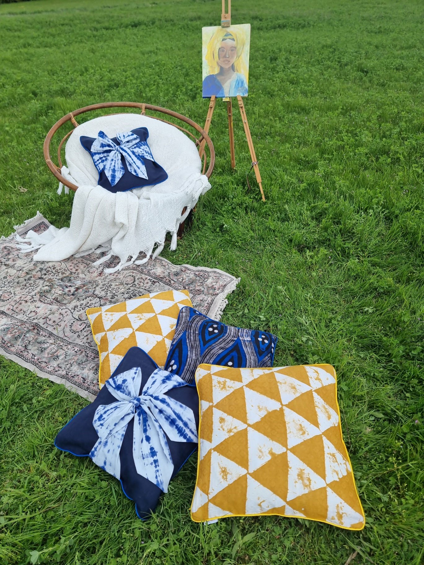 African handmade batik cushions and indigo textiles styled outdoors on a rug in a green meadow.