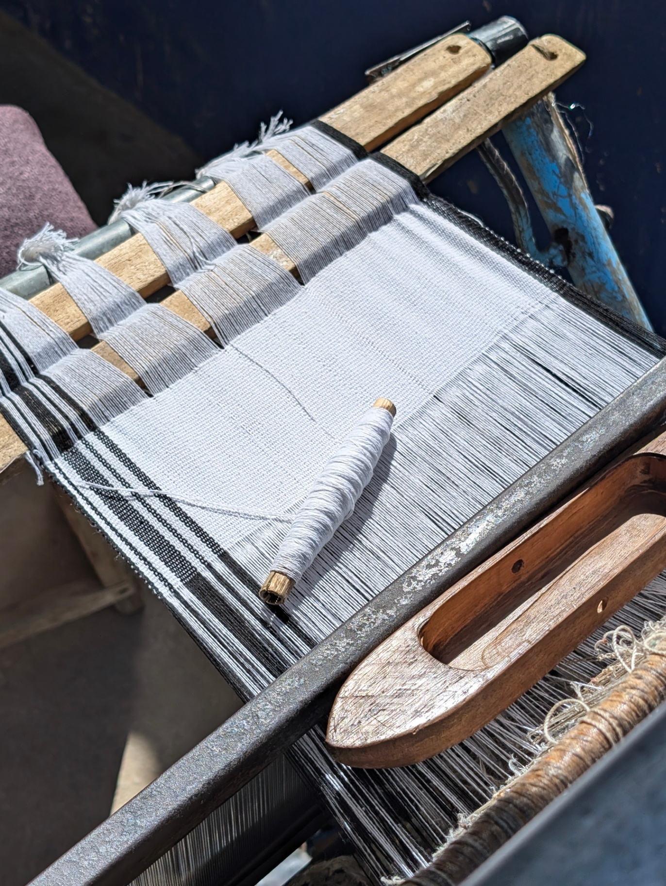 A wooden shuttle and spool resting on a traditional loom warped with white thread for smock weaving.