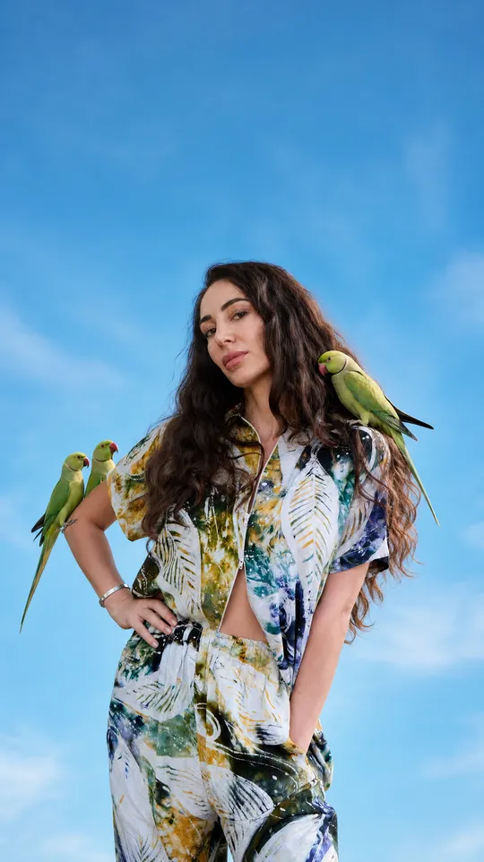 Model wearing a handprinted two-piece set, parakeets perched on her arm