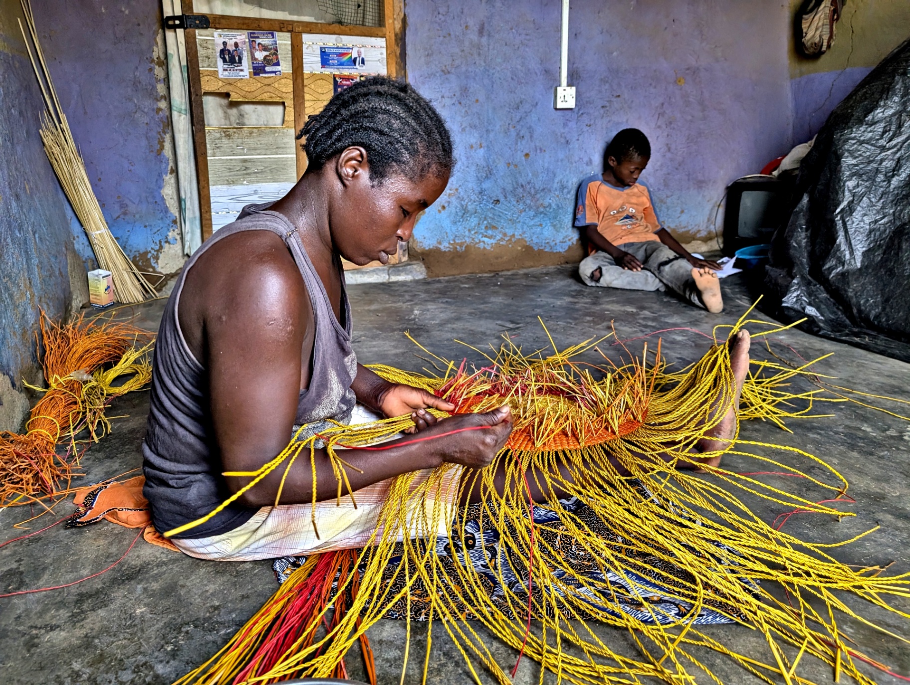 A Bolgatanga artisan weaving a basket from bright yellow and red dyed elephant grass.