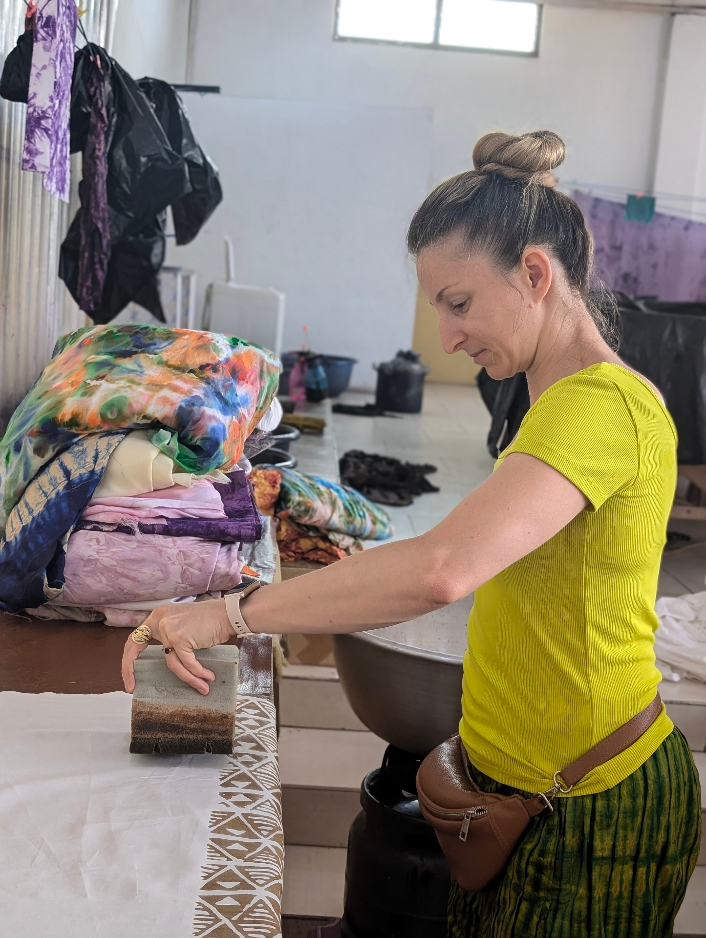 An artisan pressing a hand-carved block stamp onto white fabric in a textile workshop.