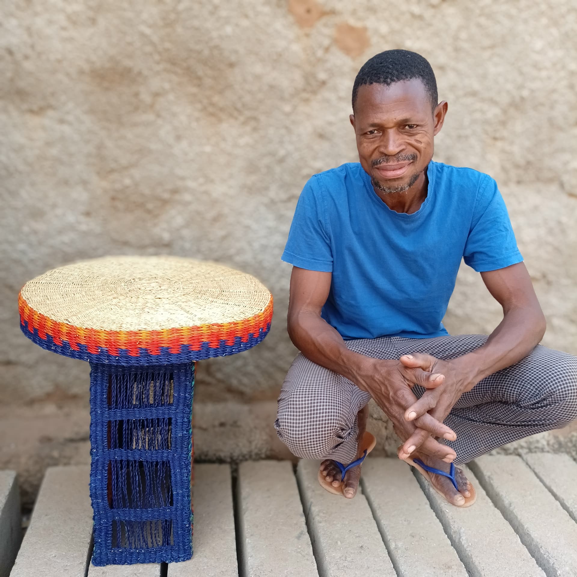 Weaver sitting beside the completed Amira table with its natural woven top and blue arch base