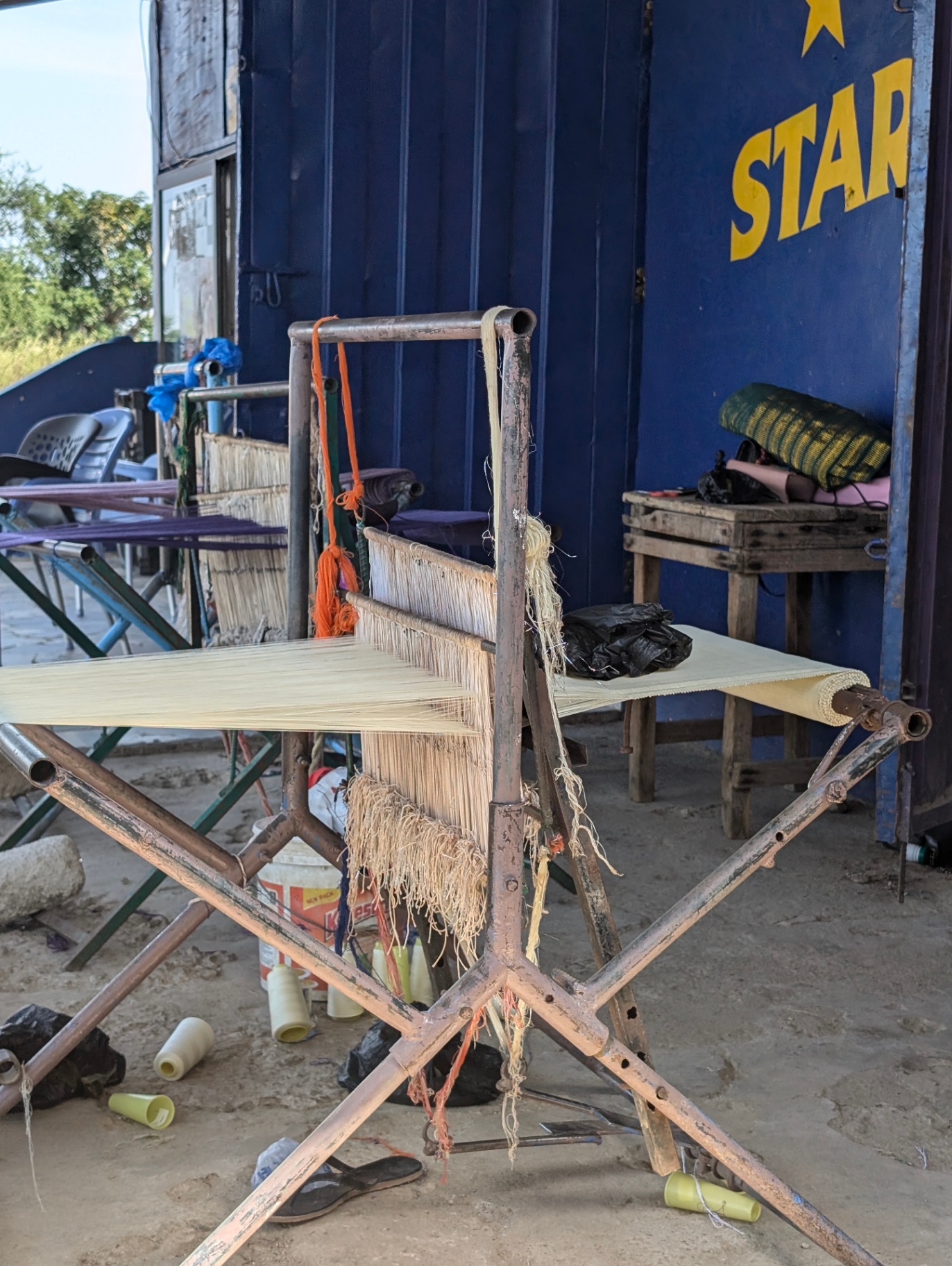 A traditional Ghanaian narrow-strip loom set up outdoors with warped cotton threads.