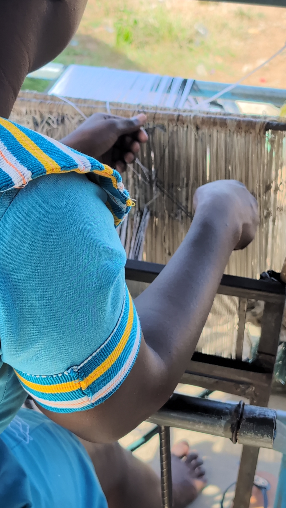 A young weaver working at a narrow-strip loom, threading the warp by hand.