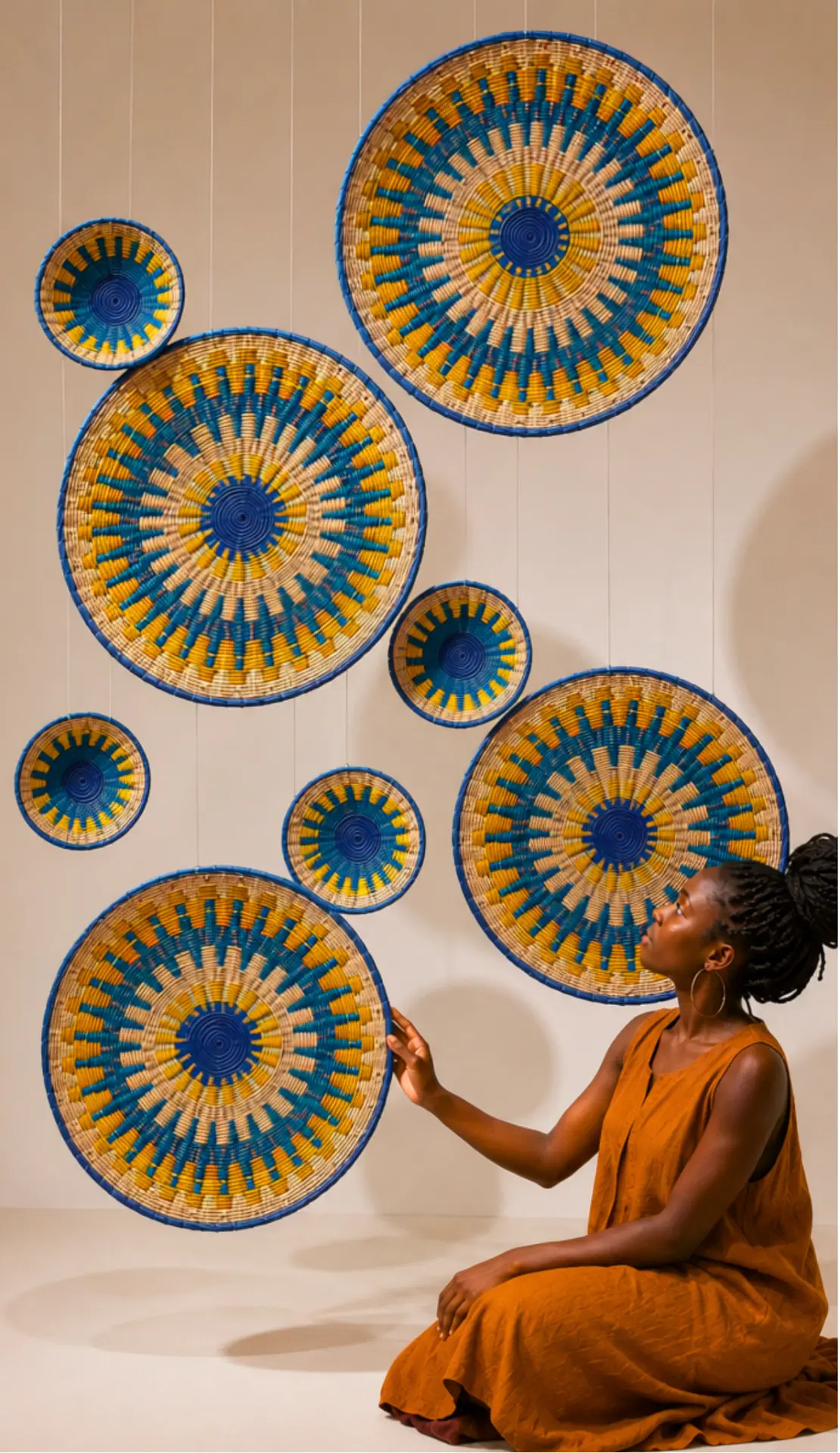 Woman beside an installation of circular woven wall baskets in indigo, turquoise and ochre