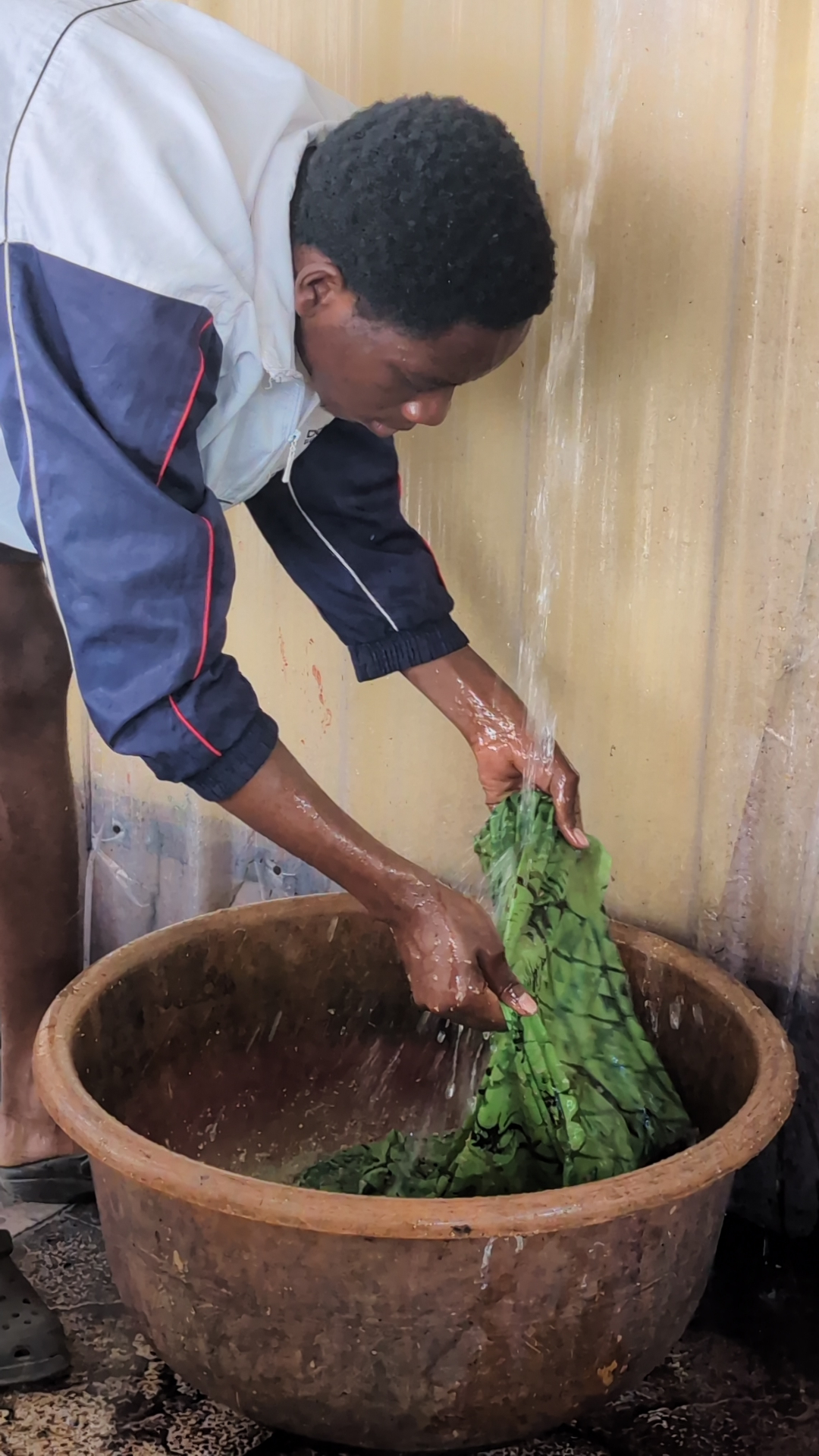 An artisan rinsing freshly dyed green batik fabric under running water in a large basin.