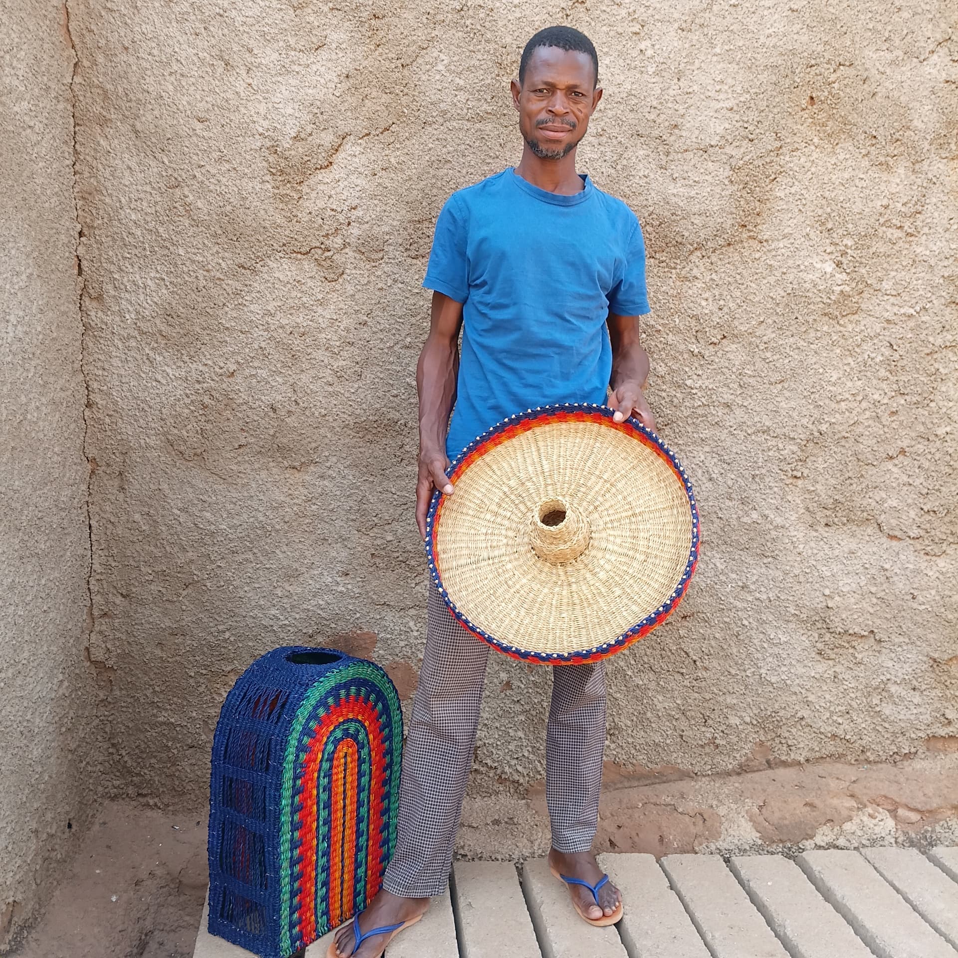 Weaver standing with the finished woven Amira top in his hands beside the rainbow-striped arch base