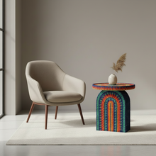 Load image into Gallery viewer, Beige armchair next to a colorful woven side table with a vase and dried plants on a neutral background
