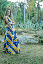 Load image into Gallery viewer, Woman in a long, patterned dress standing in a garden with cacti and palm trees.
