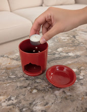 Carregar imagem no visualizador da galeria, Hand placing a candle into a red essential oil diffuser on a marble surface.
