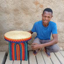 Load image into Gallery viewer, Man sitting next to a colorful woven side table with a textured wall background
