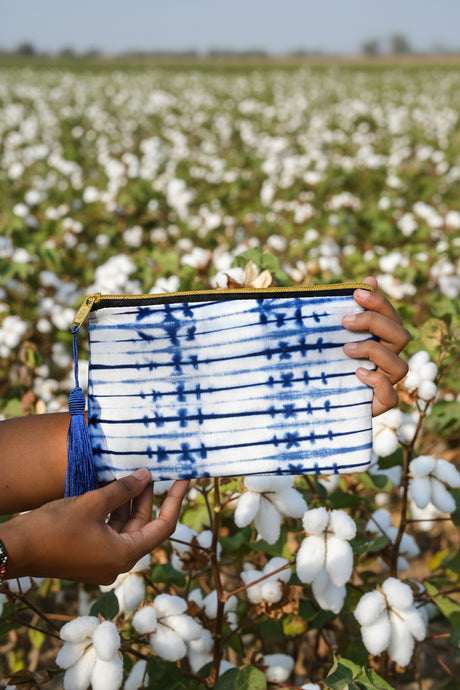 Person holding a blue and white tie-dye patterned clutch against a cotton field background