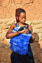 Load image into Gallery viewer, Person holding a blue bag in front of an earthen brick wall
