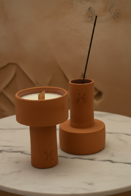 Two terracotta incense holders with a candle and incense stick on a marble surface.