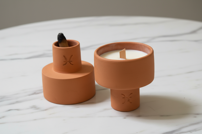 Two terracotta recipients, one with a candle, the other with an incense stick, on a marble surface