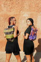 Load image into Gallery viewer, Two women wearing colorful backpacks against a textured wall.
