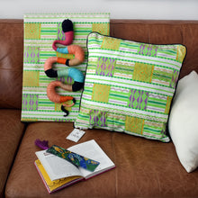 Load image into Gallery viewer, Wax Print Cushion cover with green geometric patterns, displayed on a sofa with a snake artwork.
