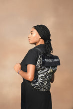 Load image into Gallery viewer, Woman wearing a black and white patterned backpack with an earthen background 
