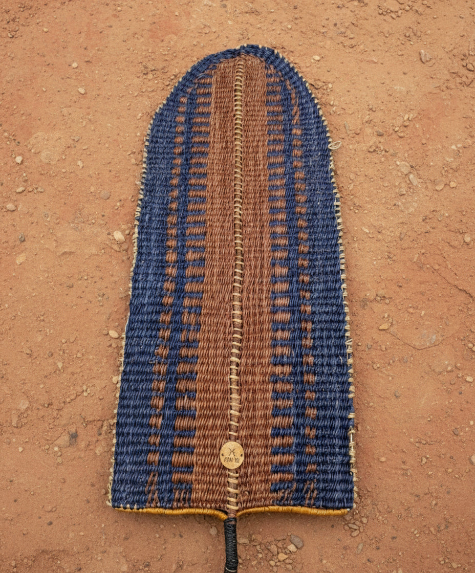 Woven blue and spice orange linear pattern on banana leaf basket laying on a dirt floor 
