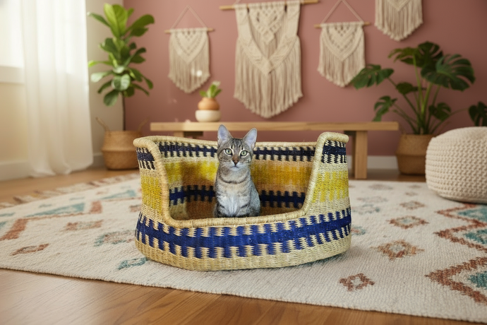 A cat sitting inside a handwoven pet basket with yellow, blue, and beige stripes.