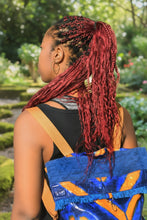 Carregar imagem no visualizador da galeria, girl with red braids wearing a blue and orange backpack in a green area
