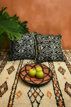 Load image into Gallery viewer, Decorative pillows with geometric batik patterns on a Moroccan wool rug with a woven bowl of apples.
